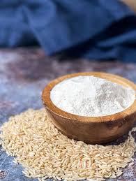 Wooden bowl with rice flour on uncooked brown rice grains in a pantry setting