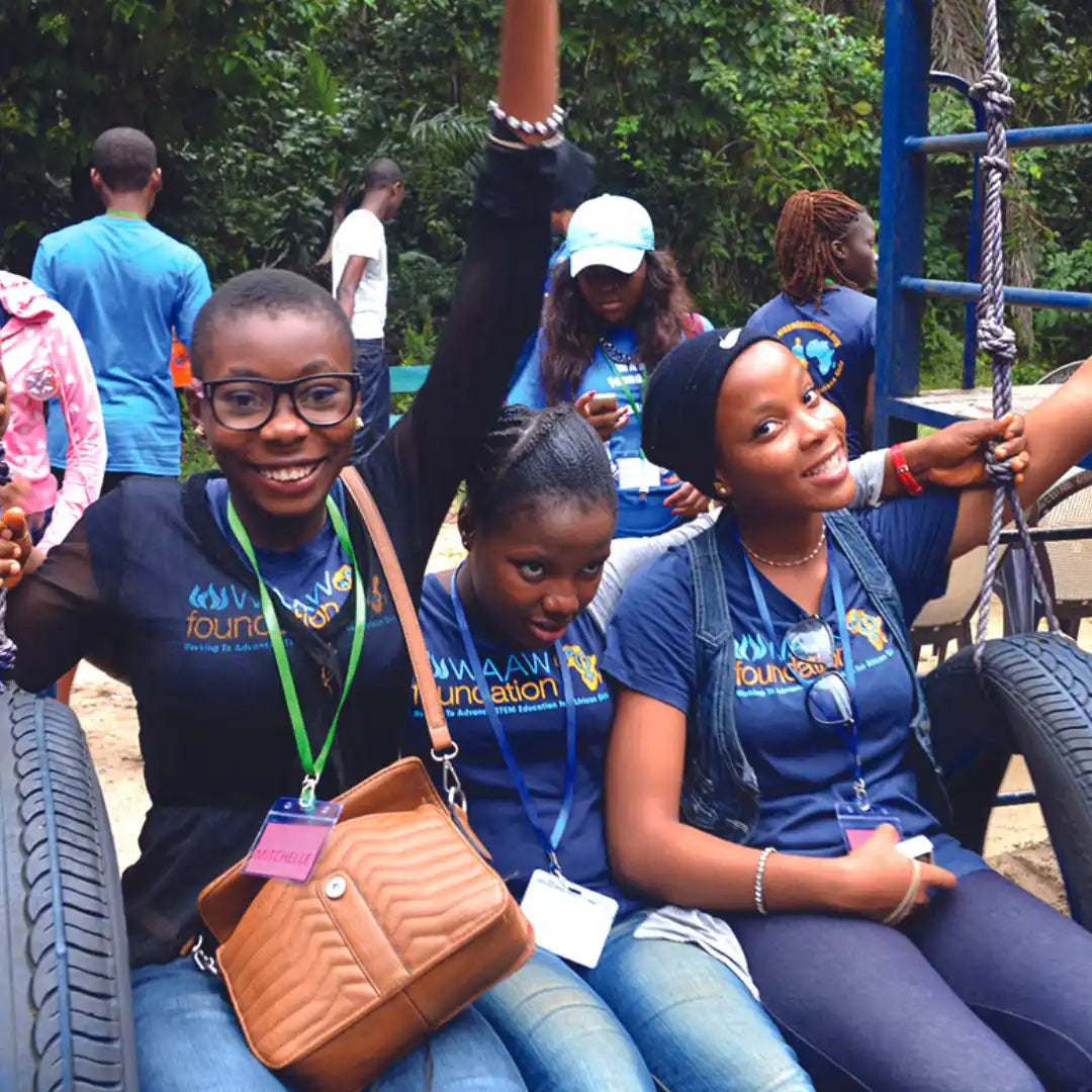 A group of smiling youth wearing matching foundation t-shirts sitting together at what appears to be an outdoor event.